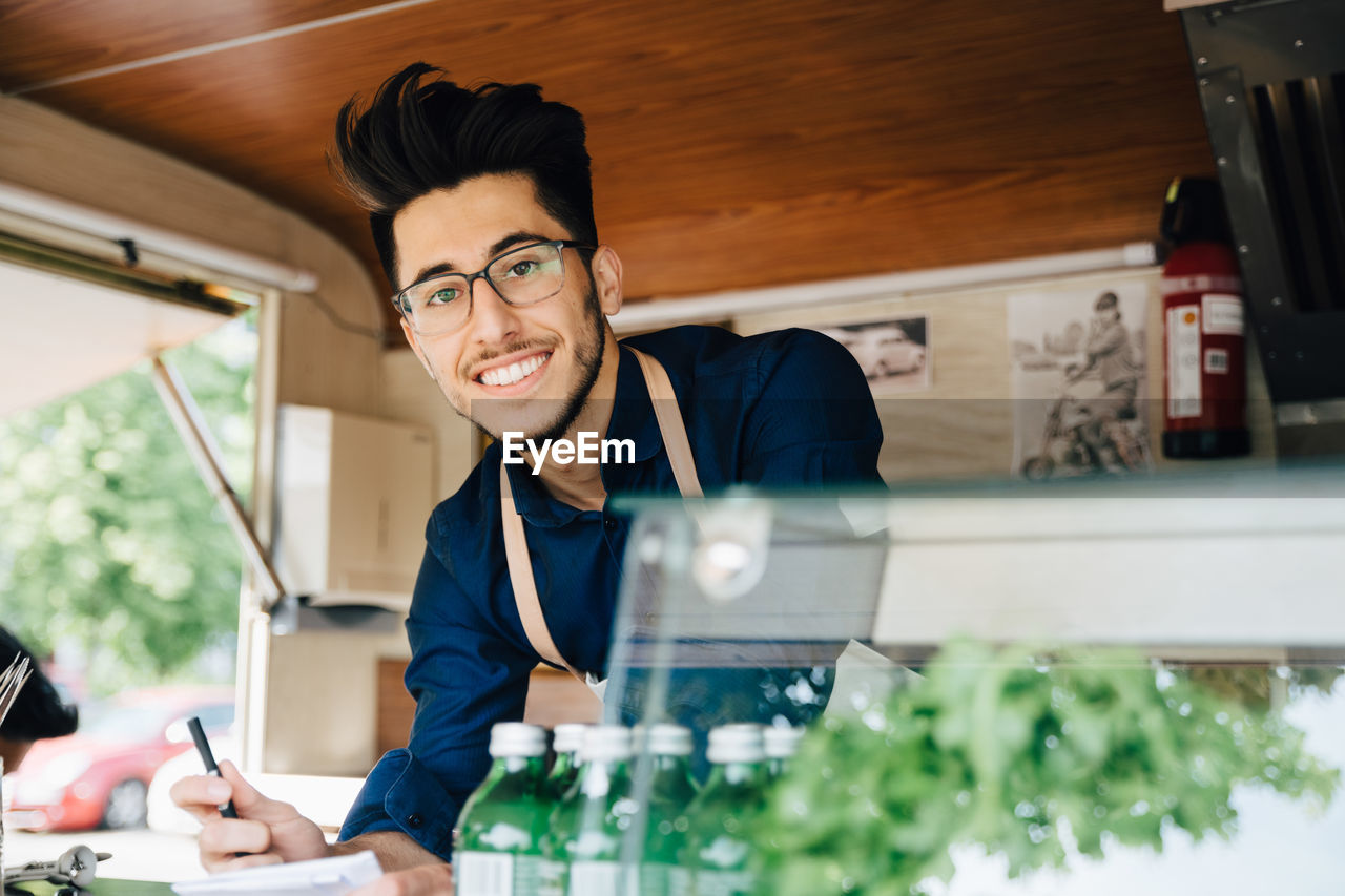 Portrait of happy male owner with pen standing in food truck