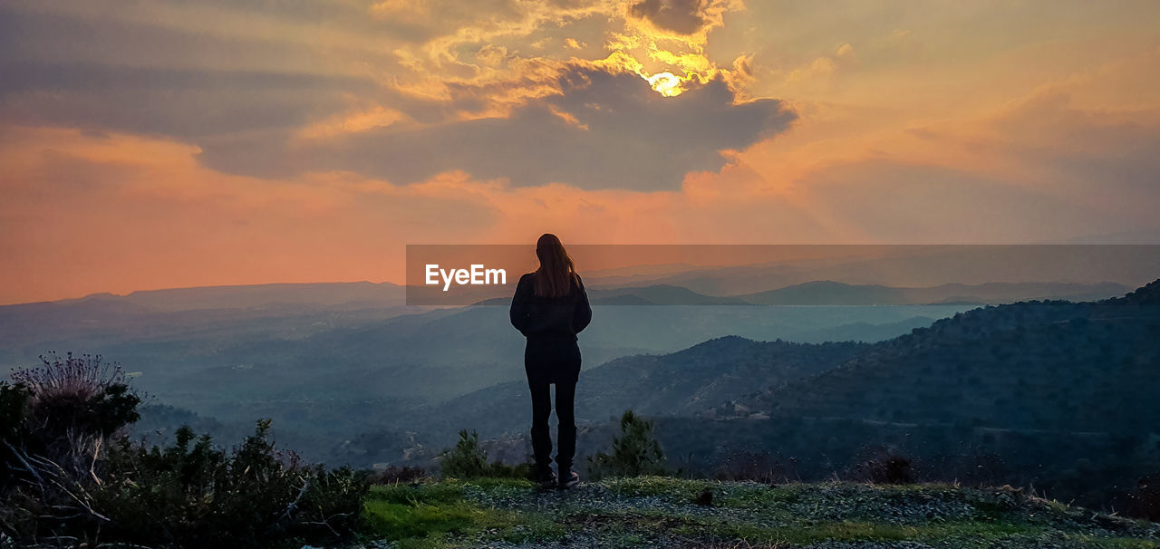 Rear view of woman standing on mountain during sunset