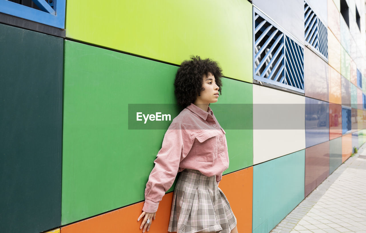 Young woman leaning on colorful wall