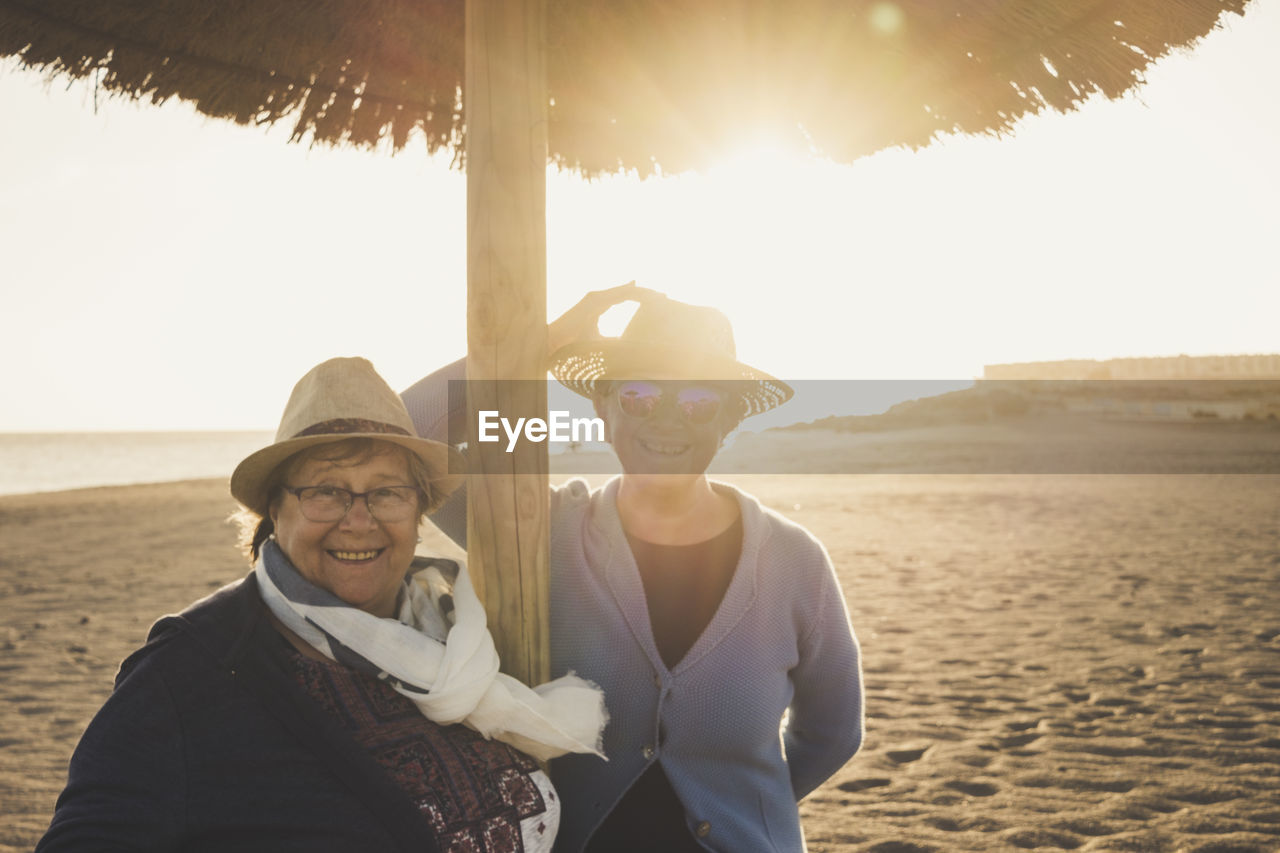 Portrait of happy friends standing at beach against clear sky