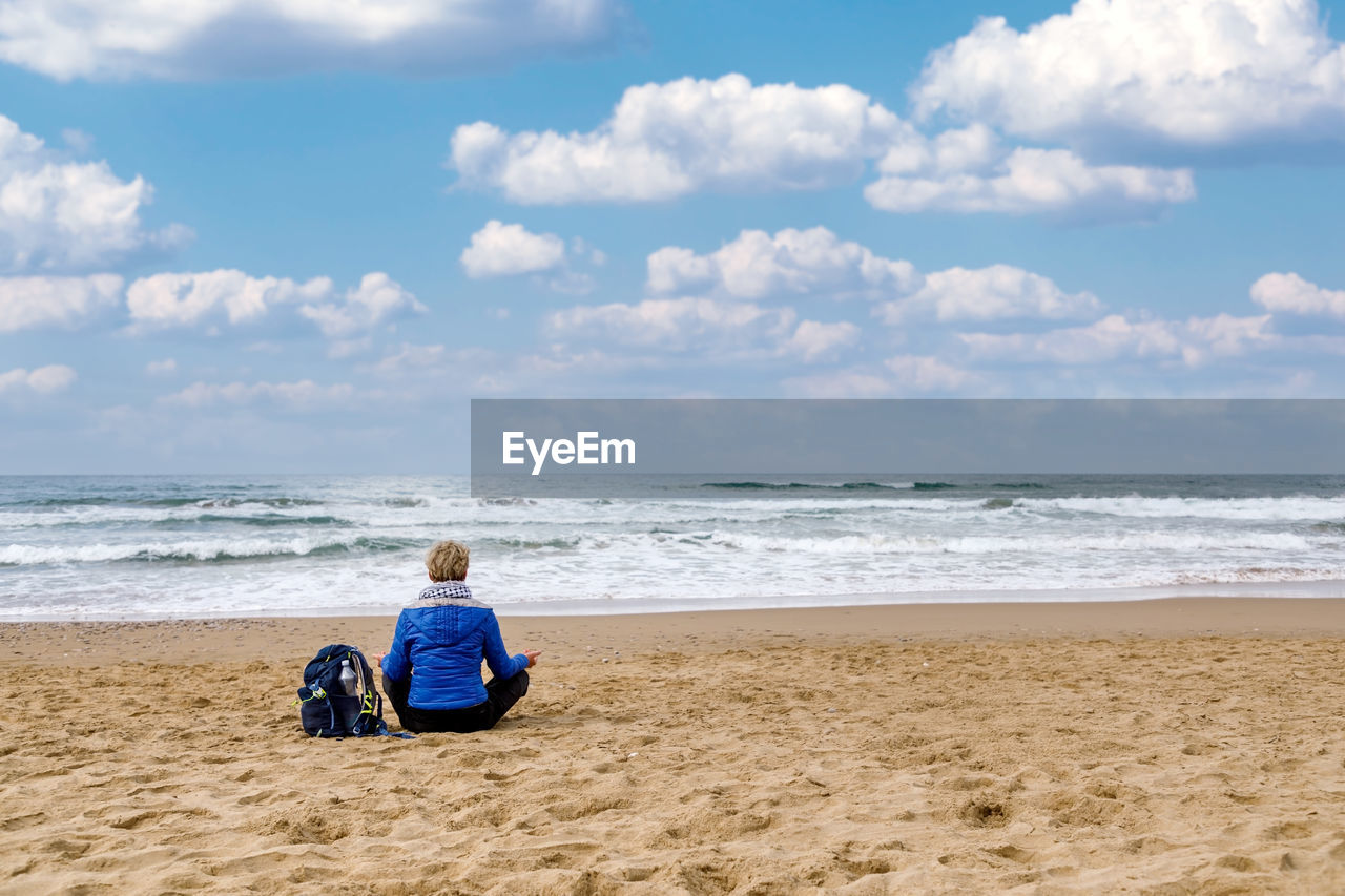 Woman sitting on the beach practicing meditation observing the horizon of the sea. 