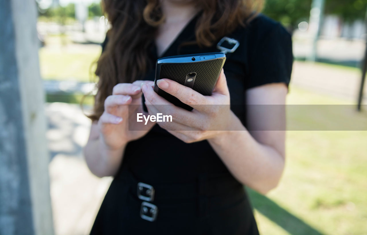 Midsection of woman using mobile phone while standing outdoors