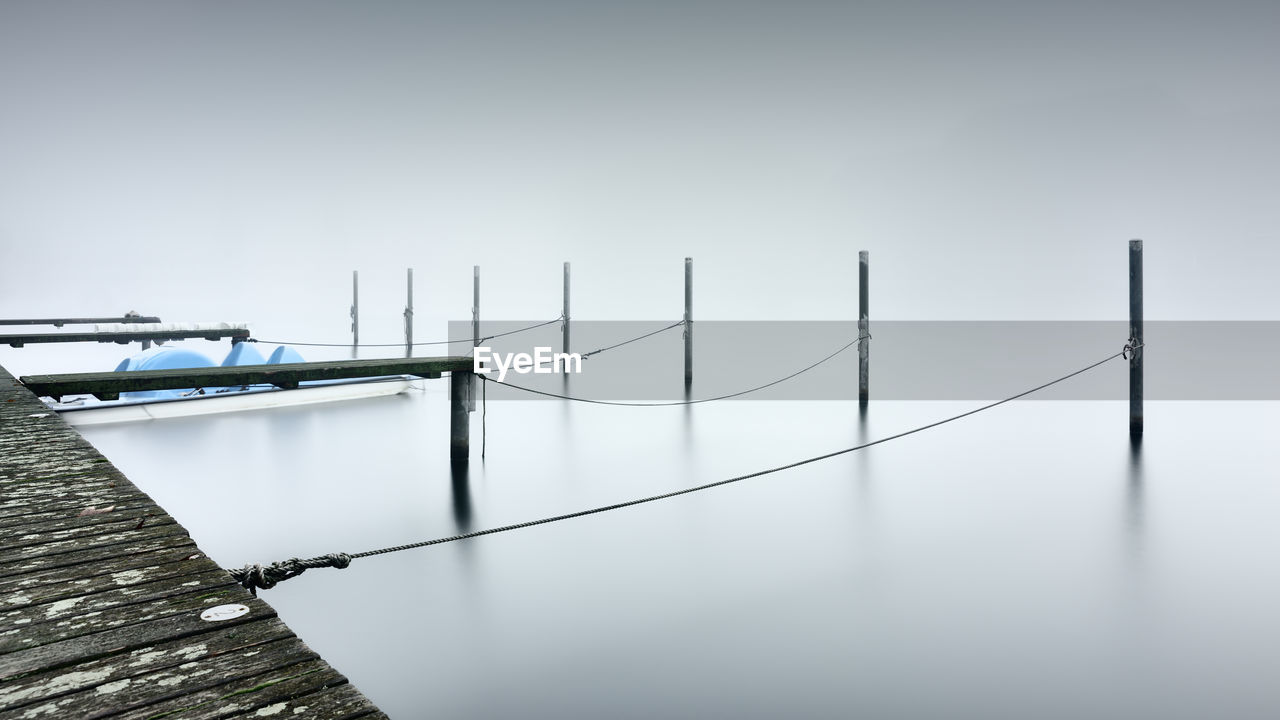 Boat moored by wooden posts tied to jetty over lake during foggy weather
