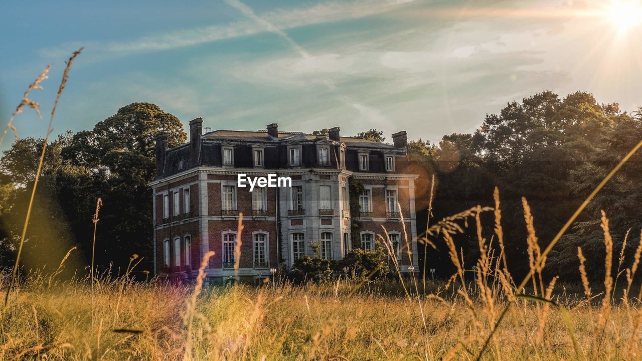 ABANDONED BUILDINGS ON FIELD AGAINST BRIGHT SUN