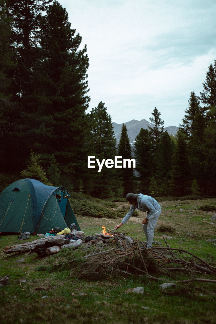 Side view of person preparing bonfire by tent