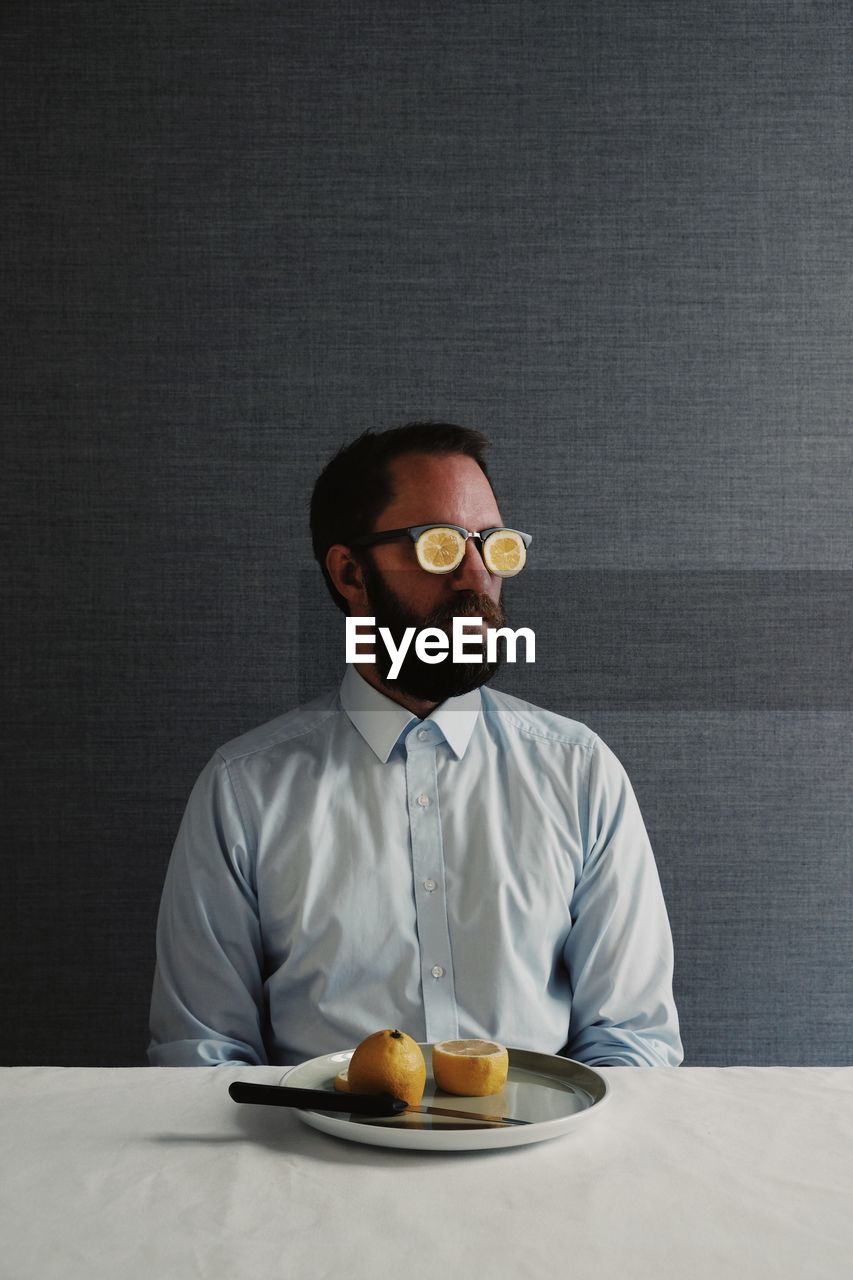 Man wearing eyeglasses sitting at table against gray wall