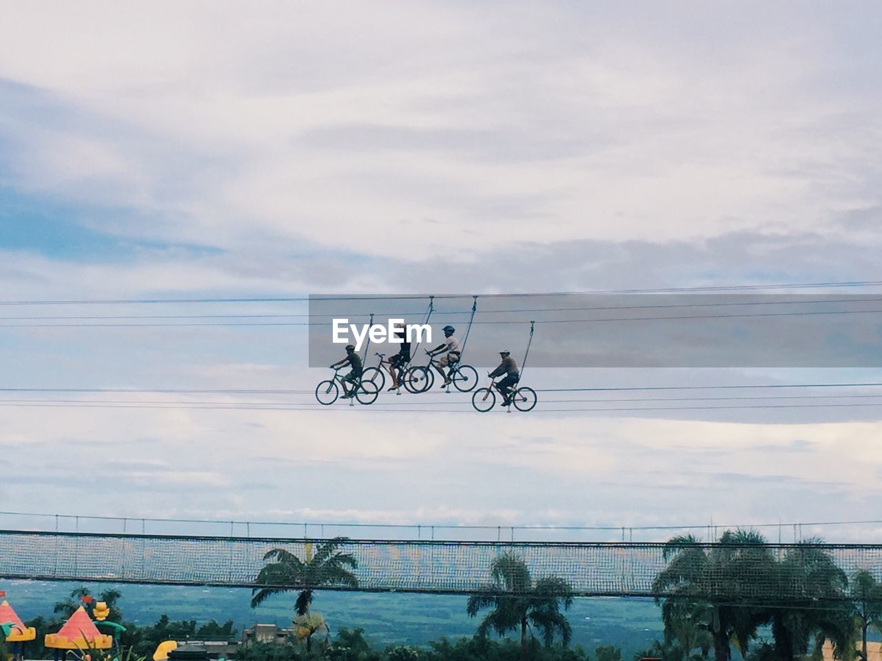 Low angle view of people zip line cycling against sky