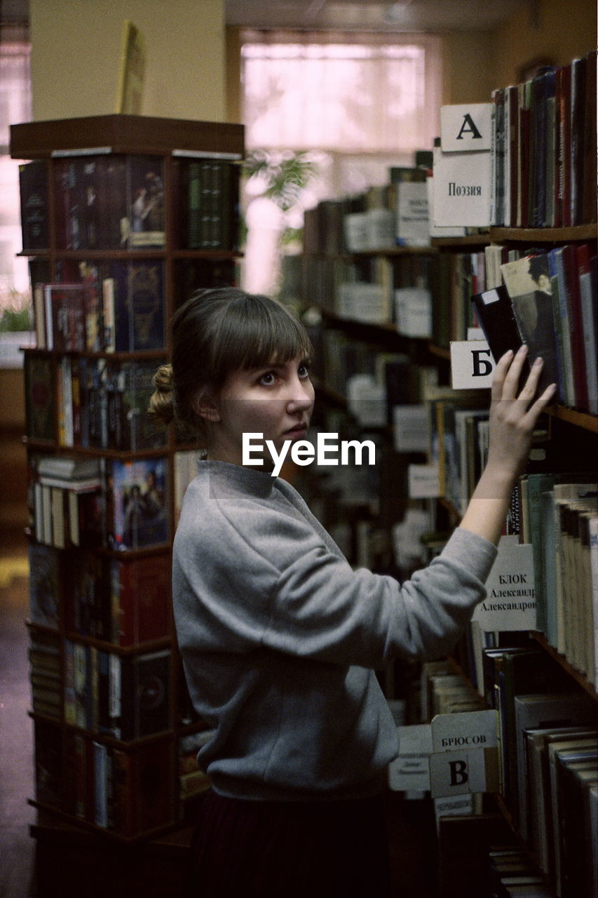 Side view of young woman searching book while standing in library