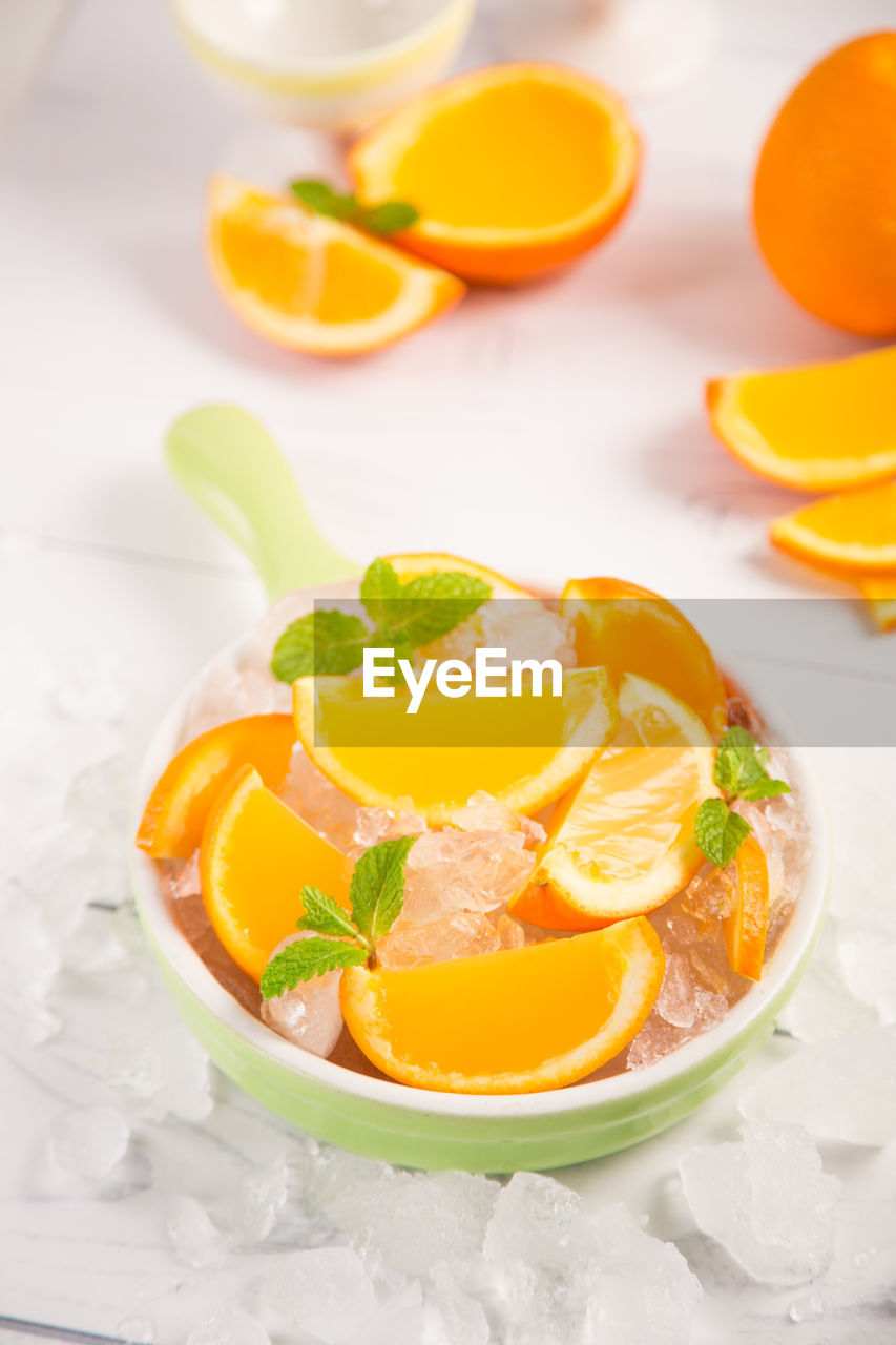 High angle view of orange fruits with ice in bowl on table