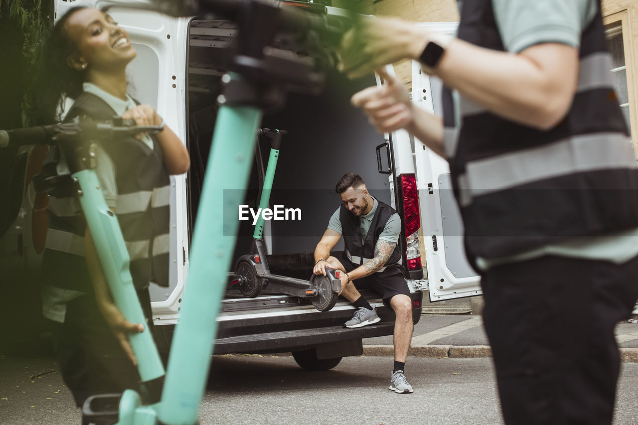 Smiling female and male workers loading electric push scooters in delivery van