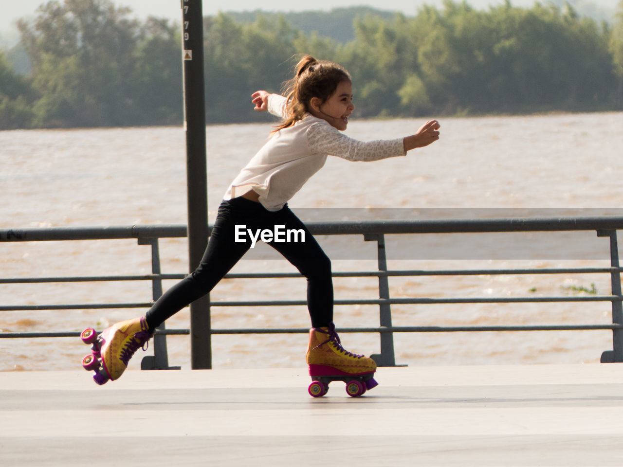 Girl roller skating on footpath against lake