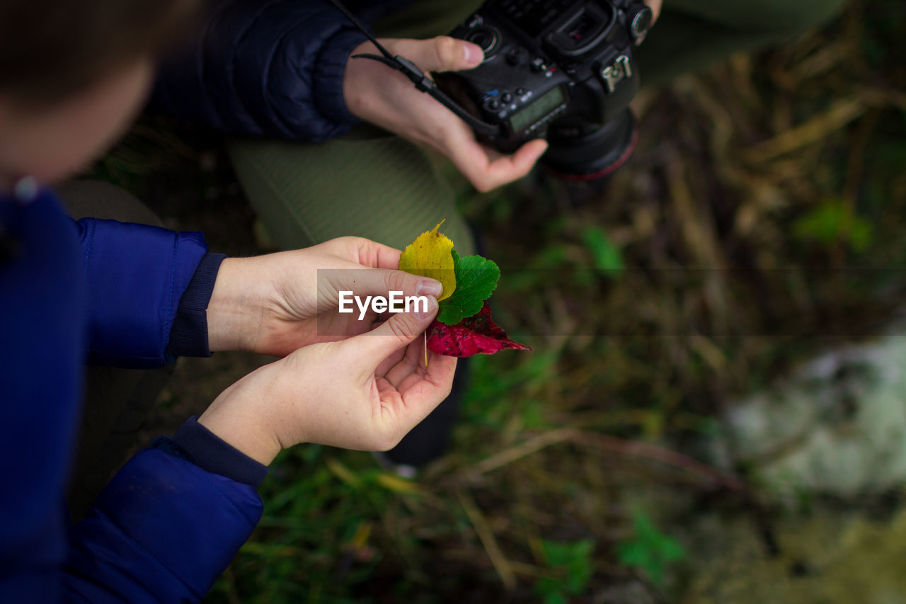 Midsection of woman holding leaves while male friend photographing with camera on field