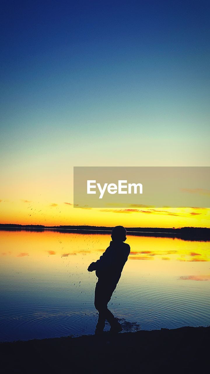 SILHOUETTE OF MAN ON BEACH AGAINST SKY DURING SUNSET