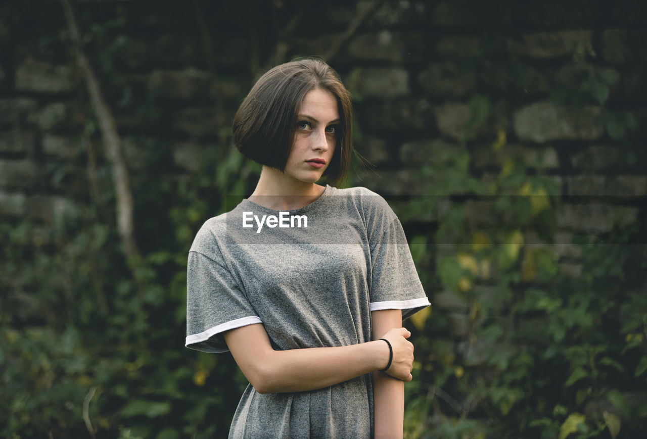 Portrait of young woman standing against wall