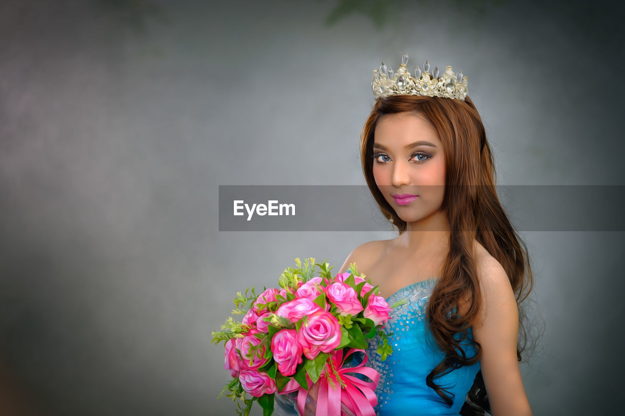 Portrait of beautiful young woman holding bouquet while standing against gray background