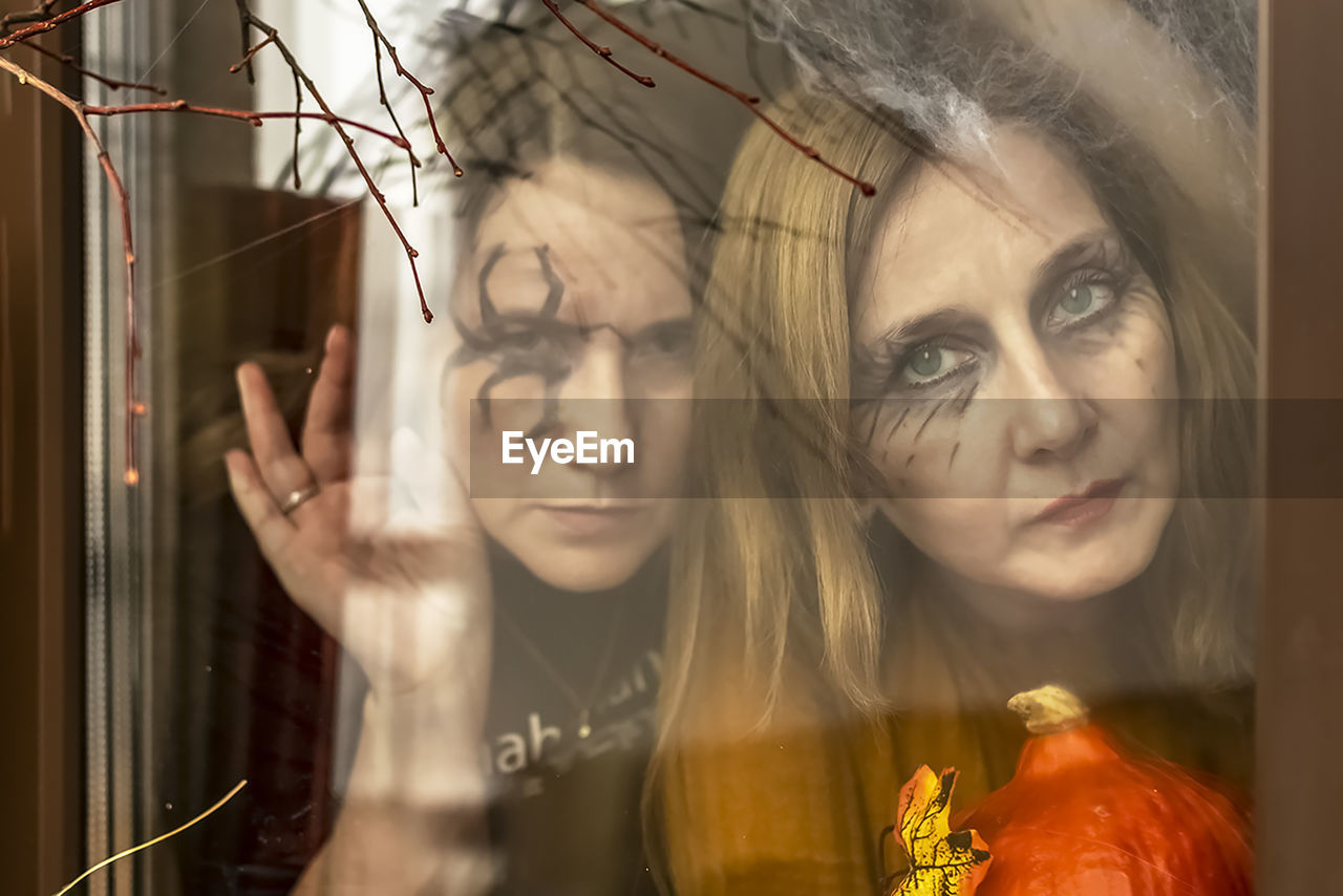 Two female witches look through a spider web ominously out of the window .halloween party.