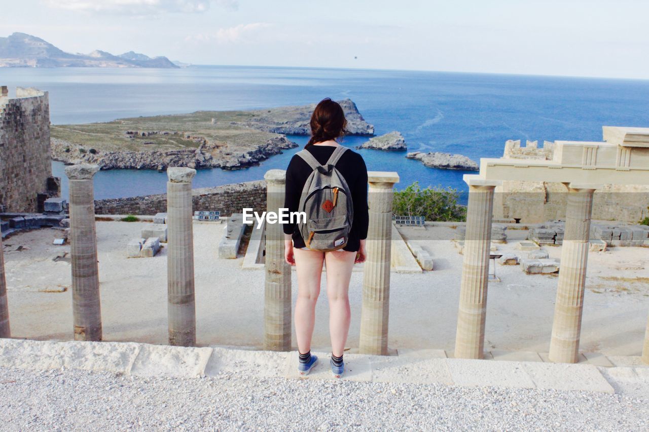 Rear view of woman standing on ruines against sky