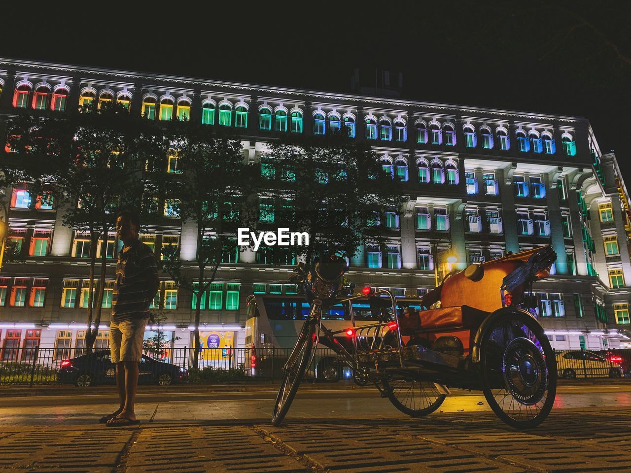 BICYCLES ON ROAD BY ILLUMINATED BUILDINGS AT NIGHT