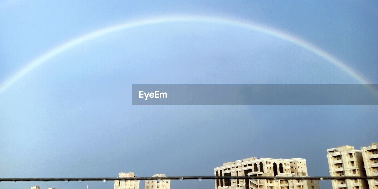 LOW ANGLE VIEW OF RAINBOW OVER BUILDINGS IN CITY AGAINST SKY