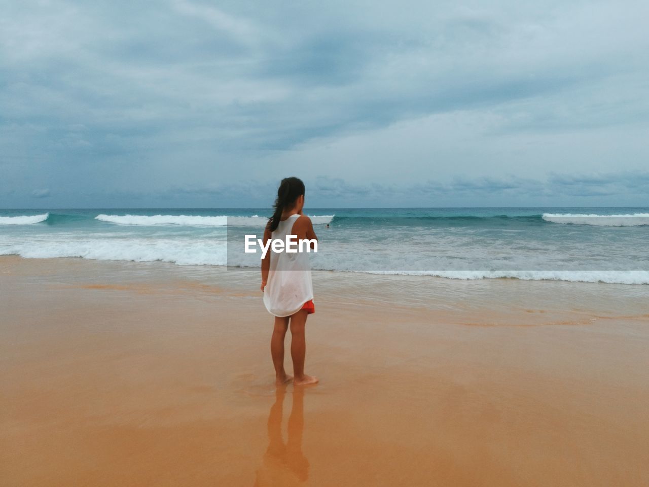 Rear view of girl standing at beach against sky