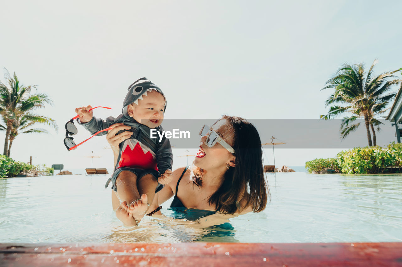 Smiling mother with son in swimming pool against sky