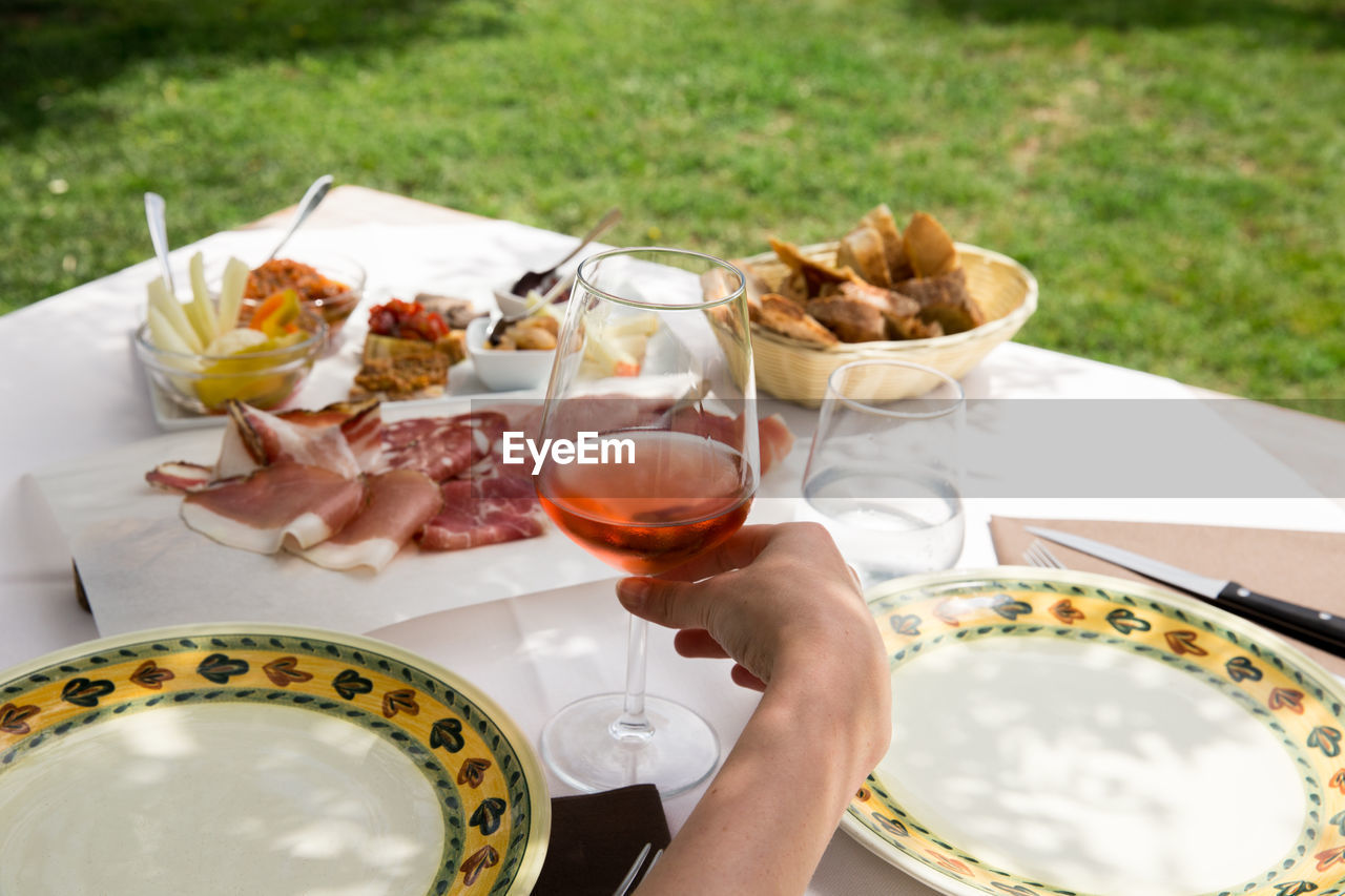 Cropped image of hand holding wine glass with antipasto served on table