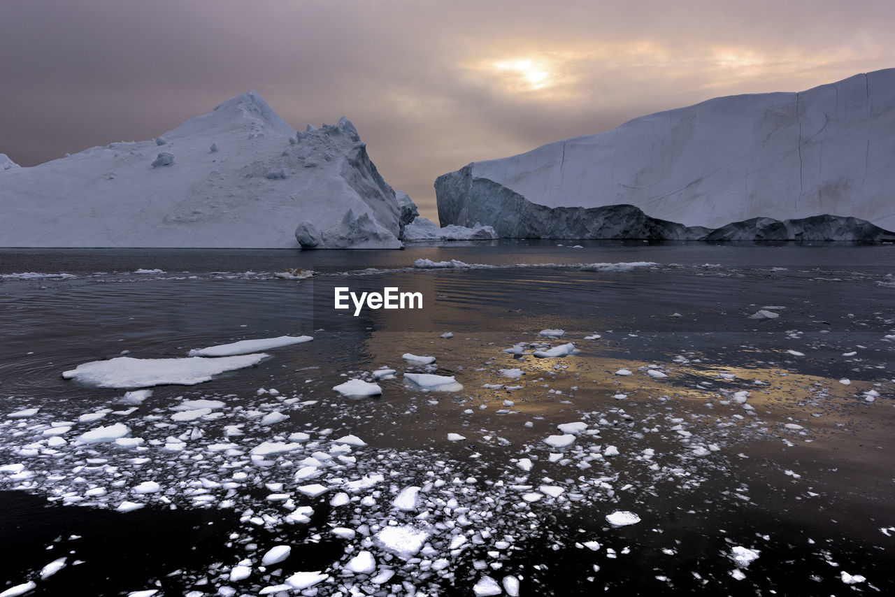 Glaciers in sea against cloudy sky during sunset