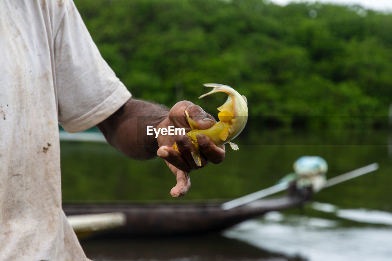 Fisherman holds yellow fish in his hand 