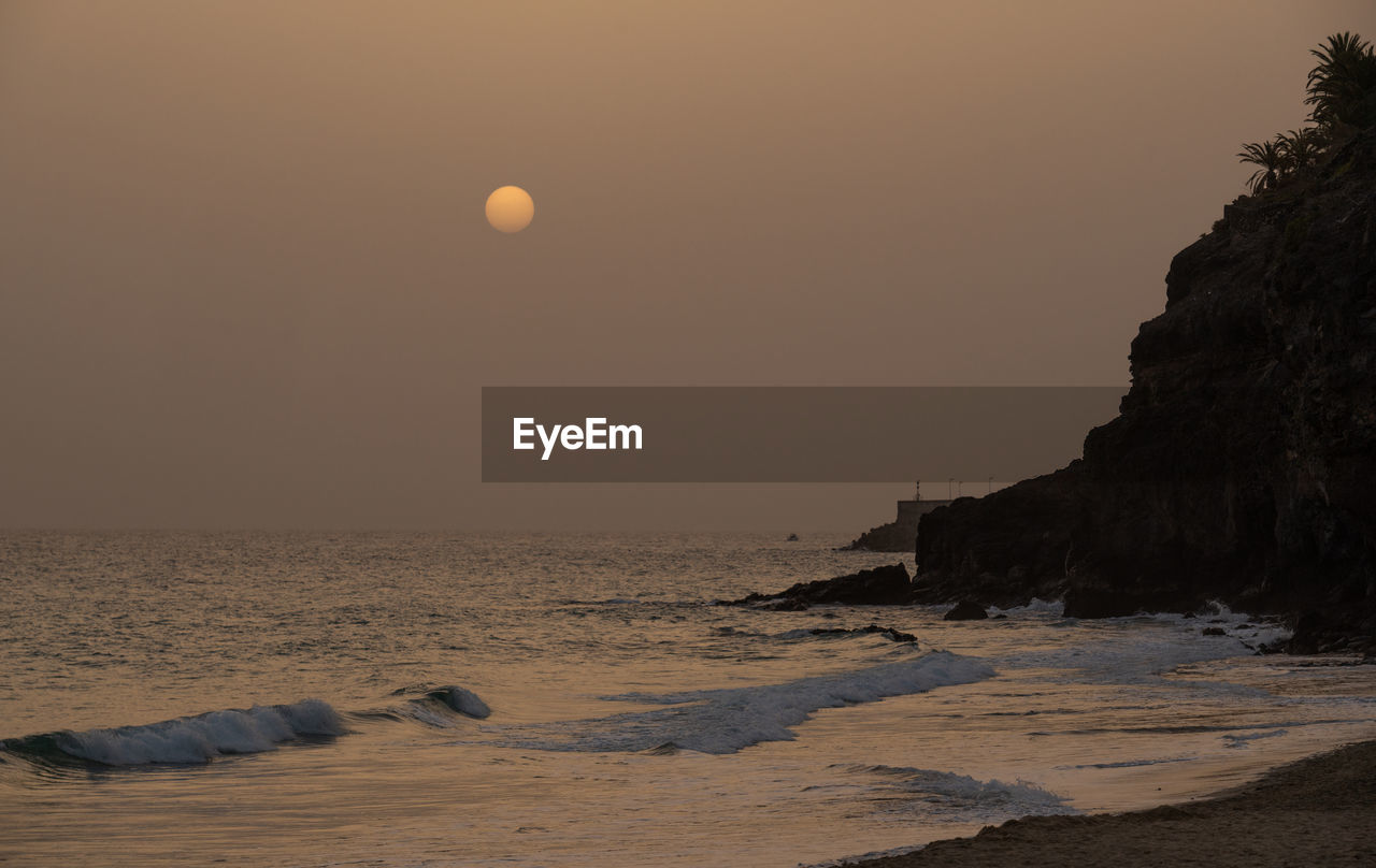 land, sea, sky, water, beach, moon, beauty in nature, ocean, scenics - nature, horizon, nature, morning, coast, tranquility, rock, sunrise, dawn, tranquil scene, wave, full moon, shore, no people, sun, environment, sand, outdoors, landscape, travel destinations, horizon over water, motion, idyllic, travel, astronomical object, body of water, seascape, coastline, non-urban scene