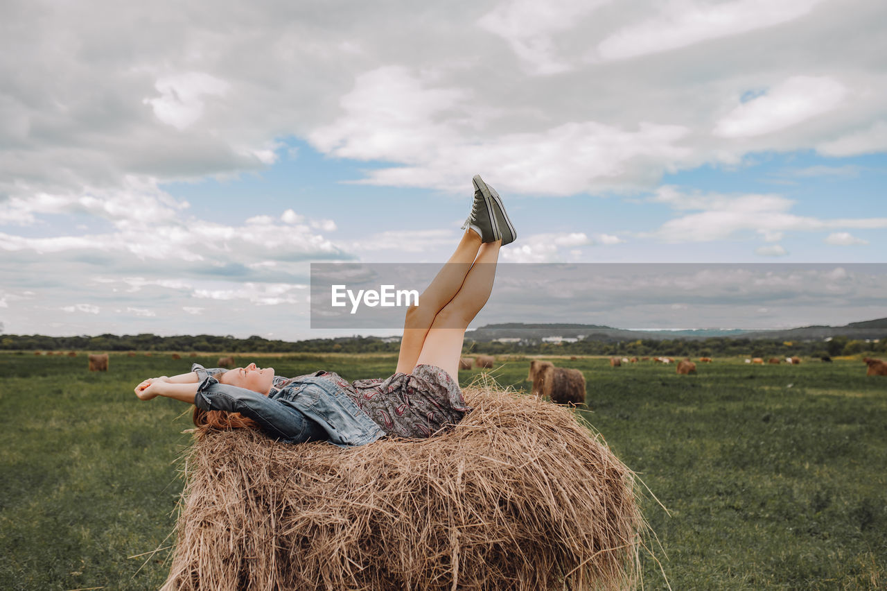 MAN RELAXING ON FIELD BY HAY BALES AGAINST SKY