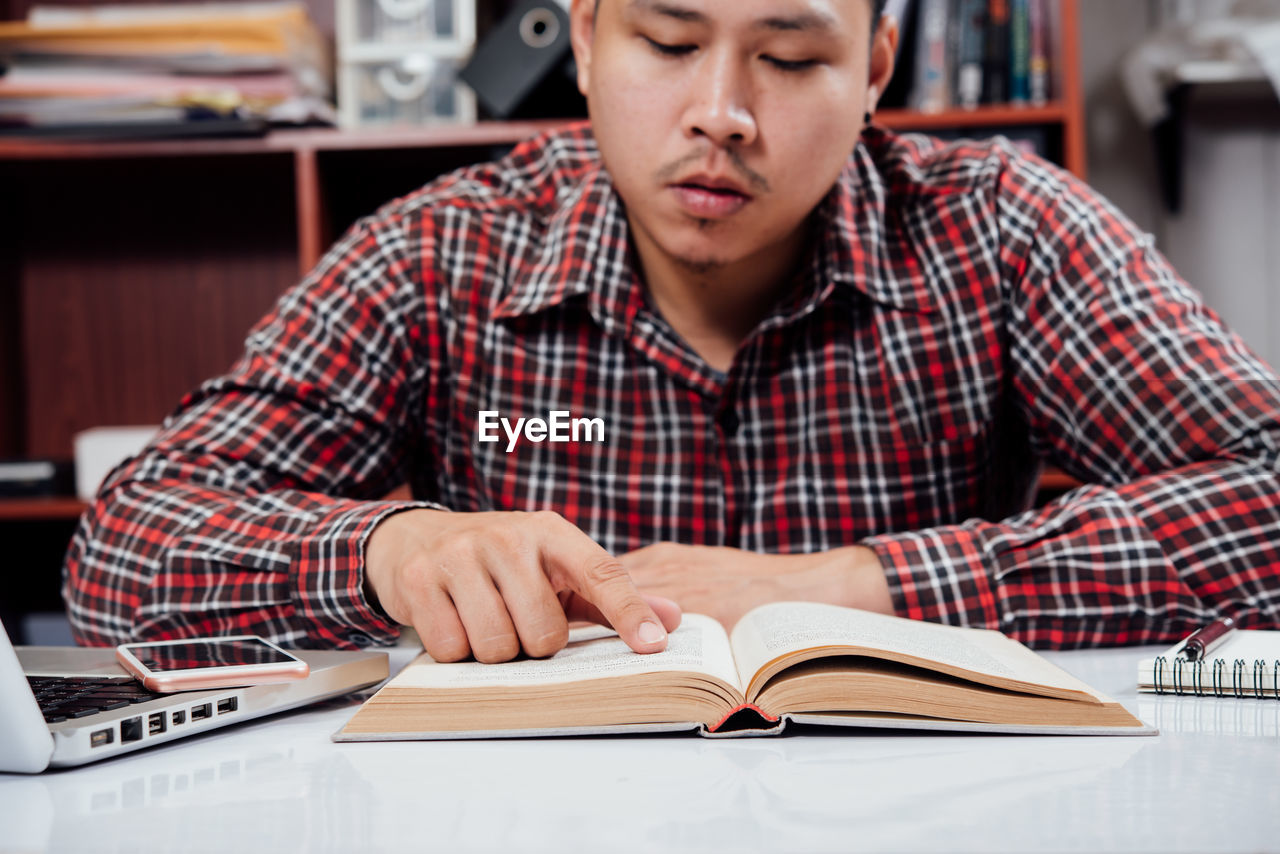 MID ADULT MAN SITTING ON TABLE AT BOOK