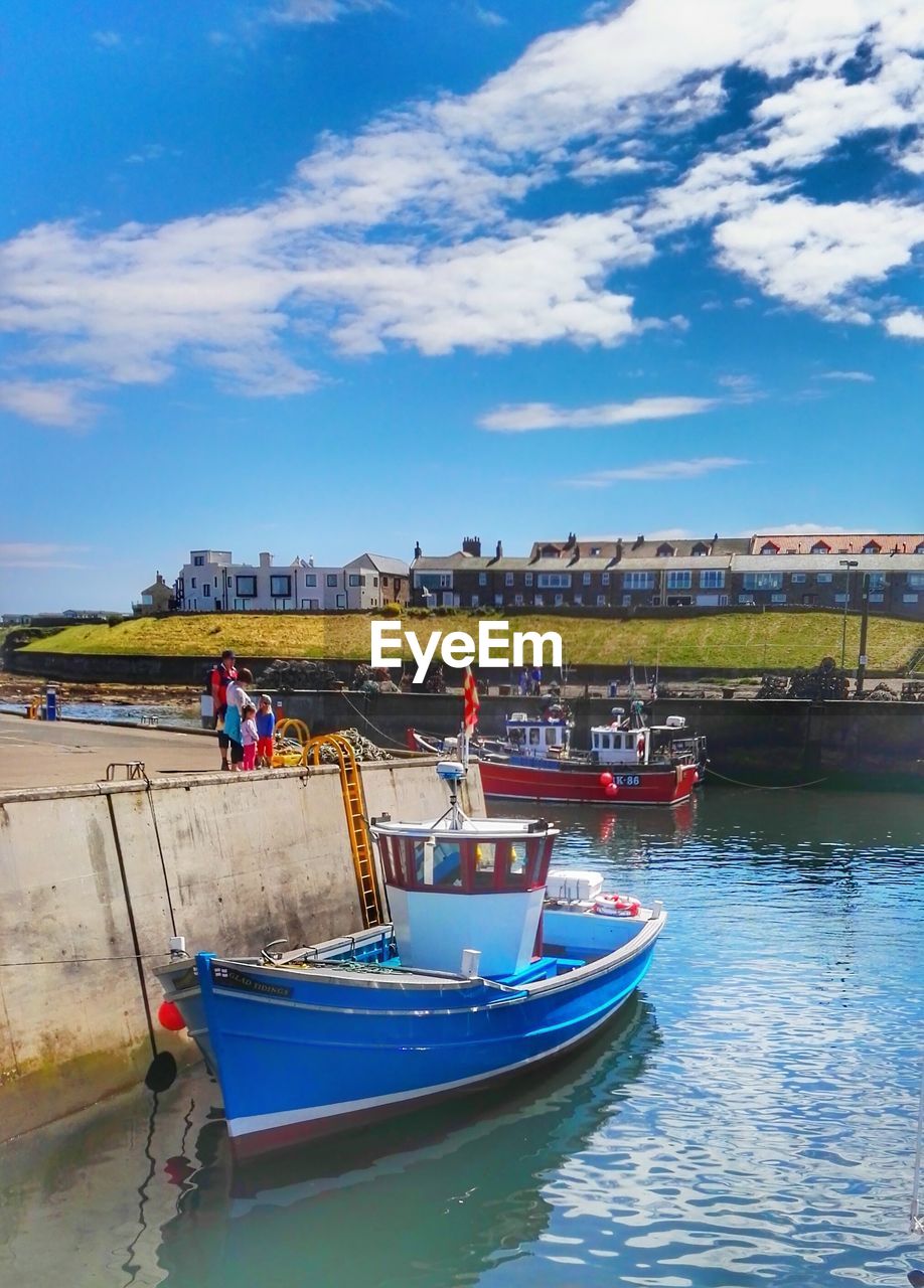 Fishing boats moored in canal at seahouses against sky