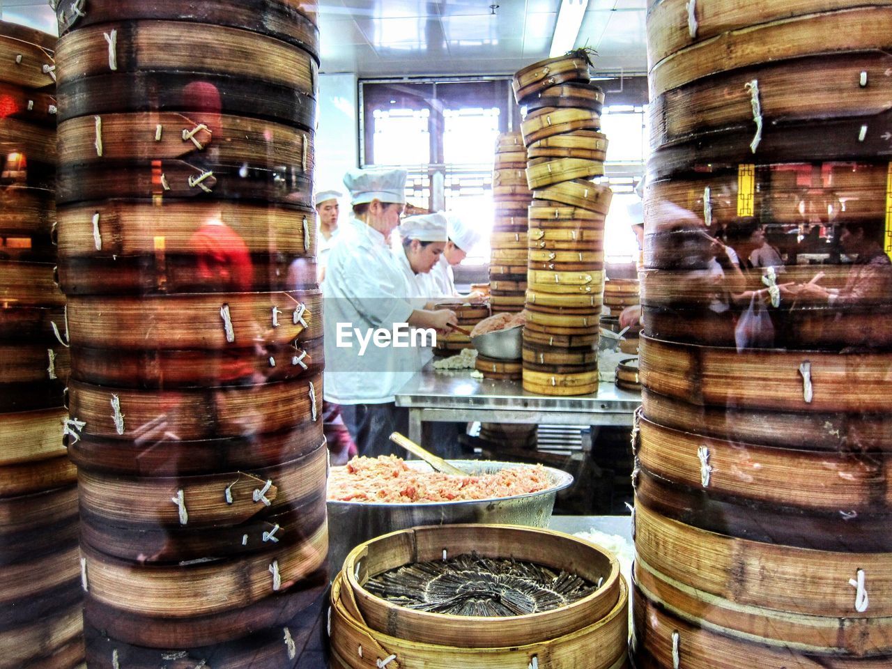 Chefs preparing dumplings by stack of wooden boxes in kitchen seen from window