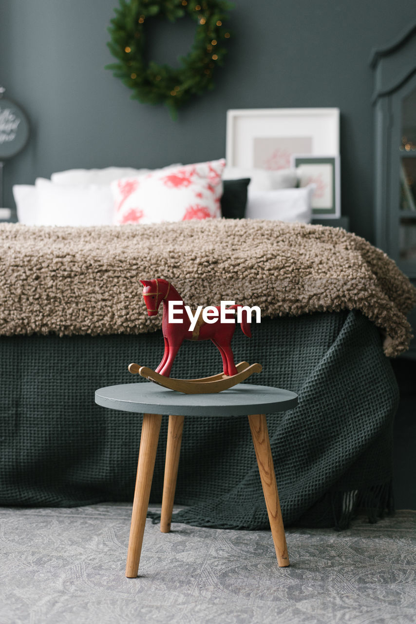 Vintage wooden toy horse stands on a stool in the christmas bedroom near the bed in dark colors