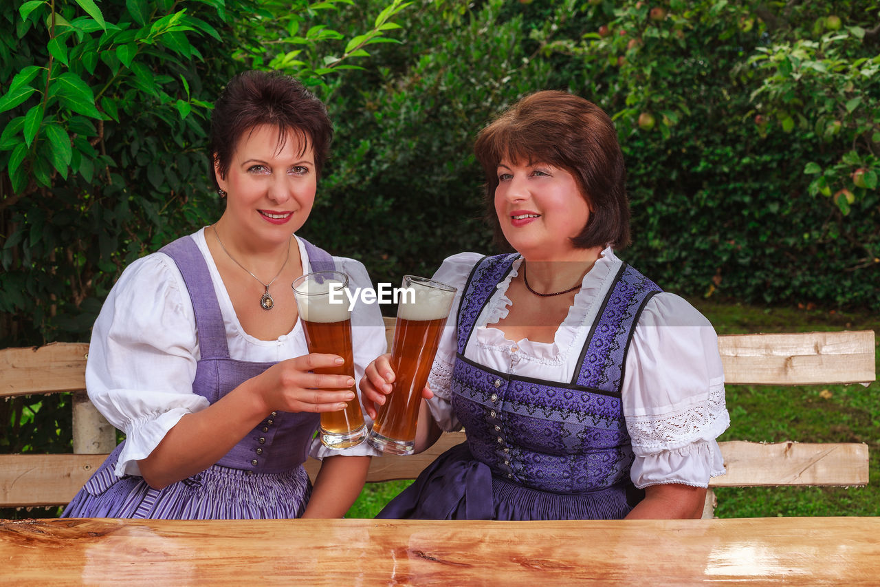 Mature female friends holding beer glasses while sitting at park