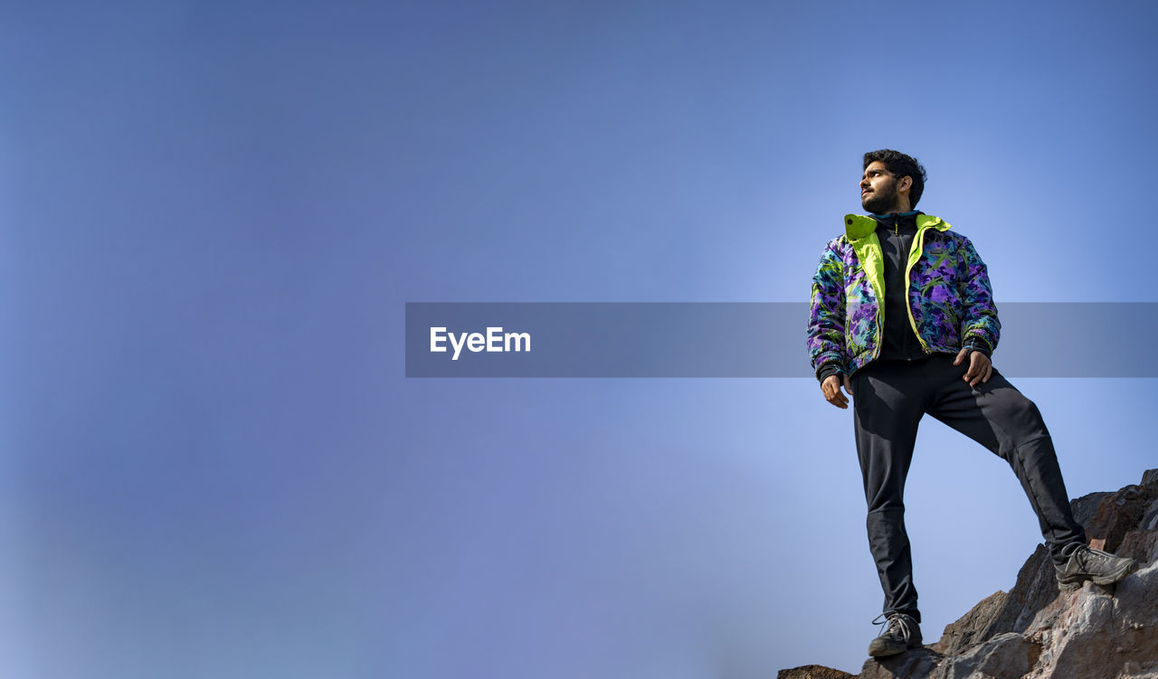 Banner of a young indian boy standing on the top of cliff wearing a snow jacket and track pants.