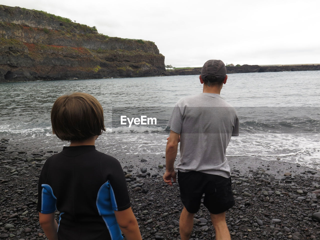 REAR VIEW OF TWO PEOPLE LOOKING AT SEA