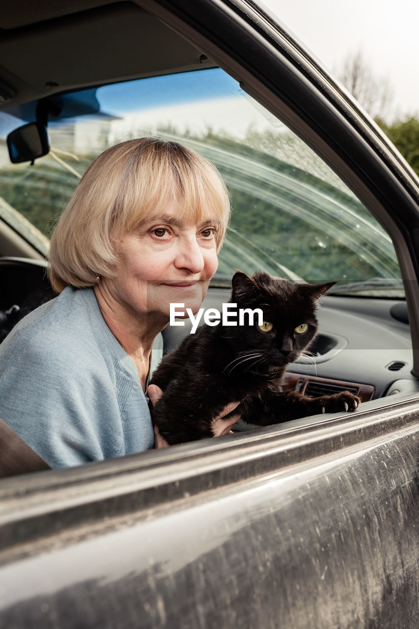 Senior adult woman holding black cat sitting in car driving to europe forced to flee from ukraine