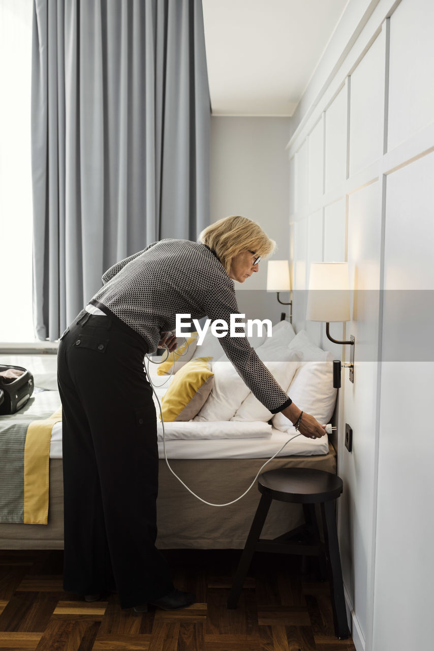 Businesswoman plugging cable by bed at hotel room