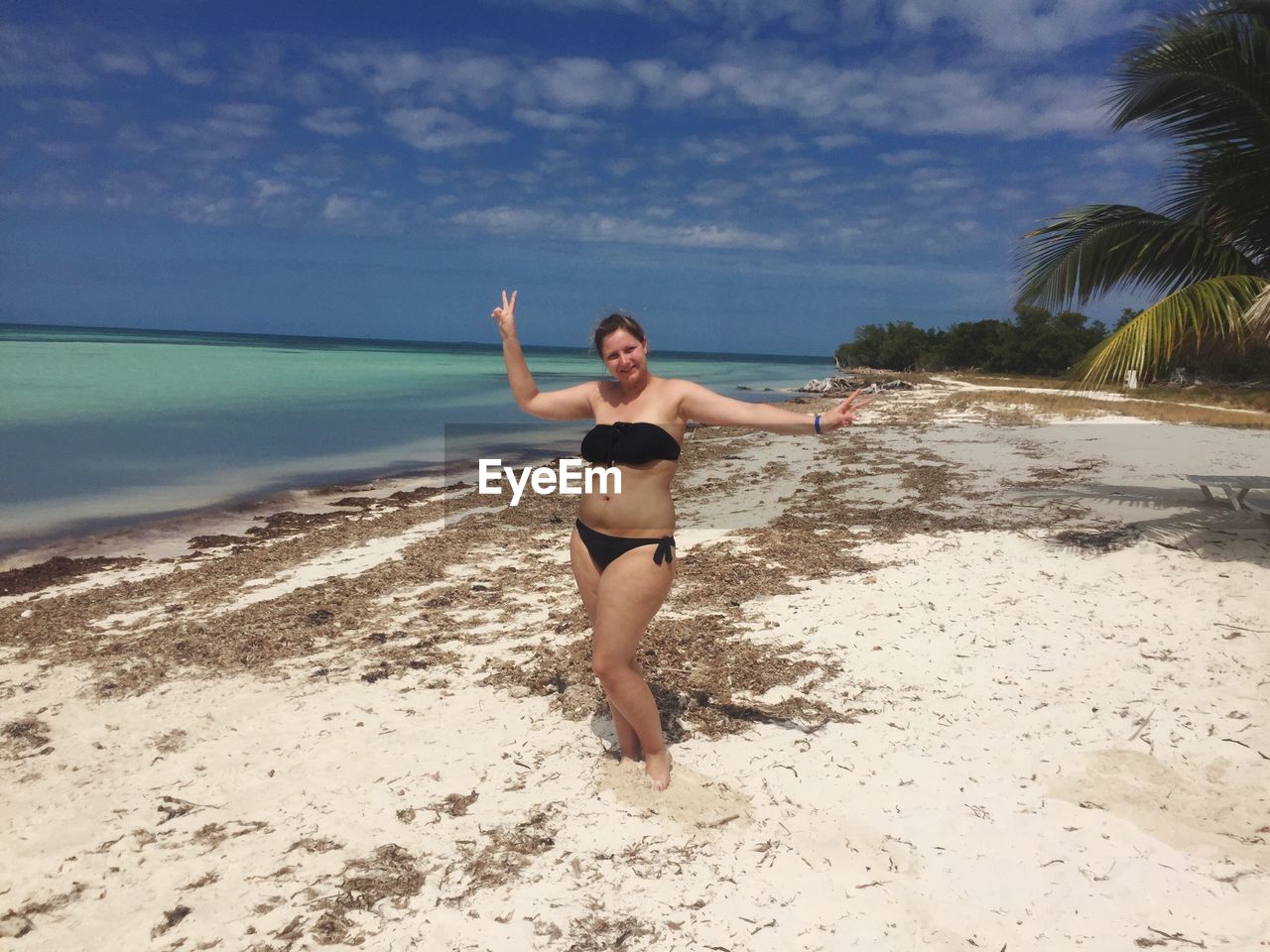 Full length of woman wearing bikini standing at beach against sky