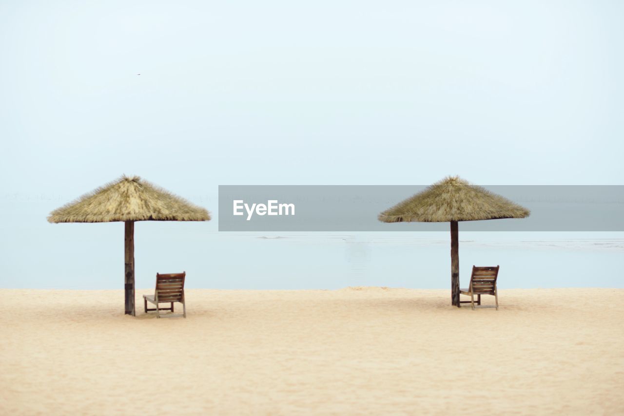 Lounge chairs by thatched roofs on sandy beach