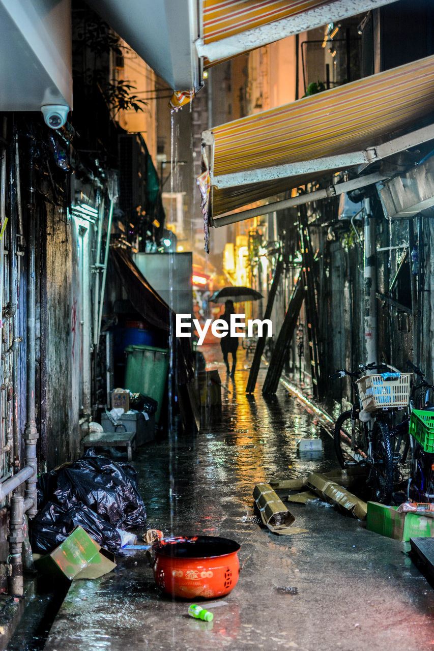 Woman with umbrella on alley amidst buildings in city at night during rainy season