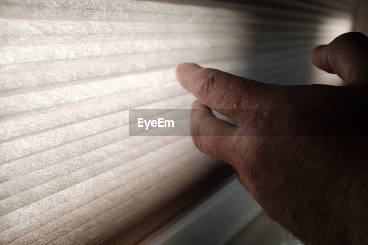 Close-up of man hand by blinds at home