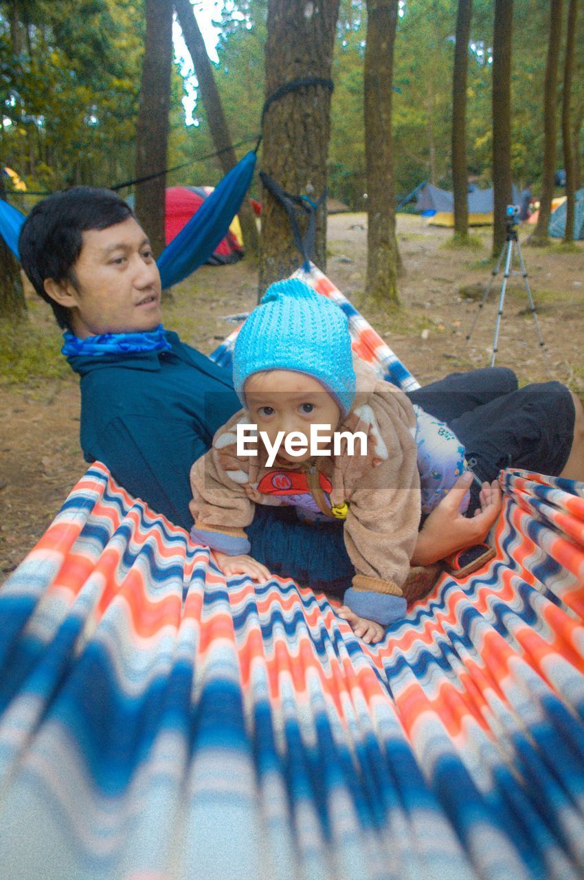 Young man with baby boy on hammock at forest