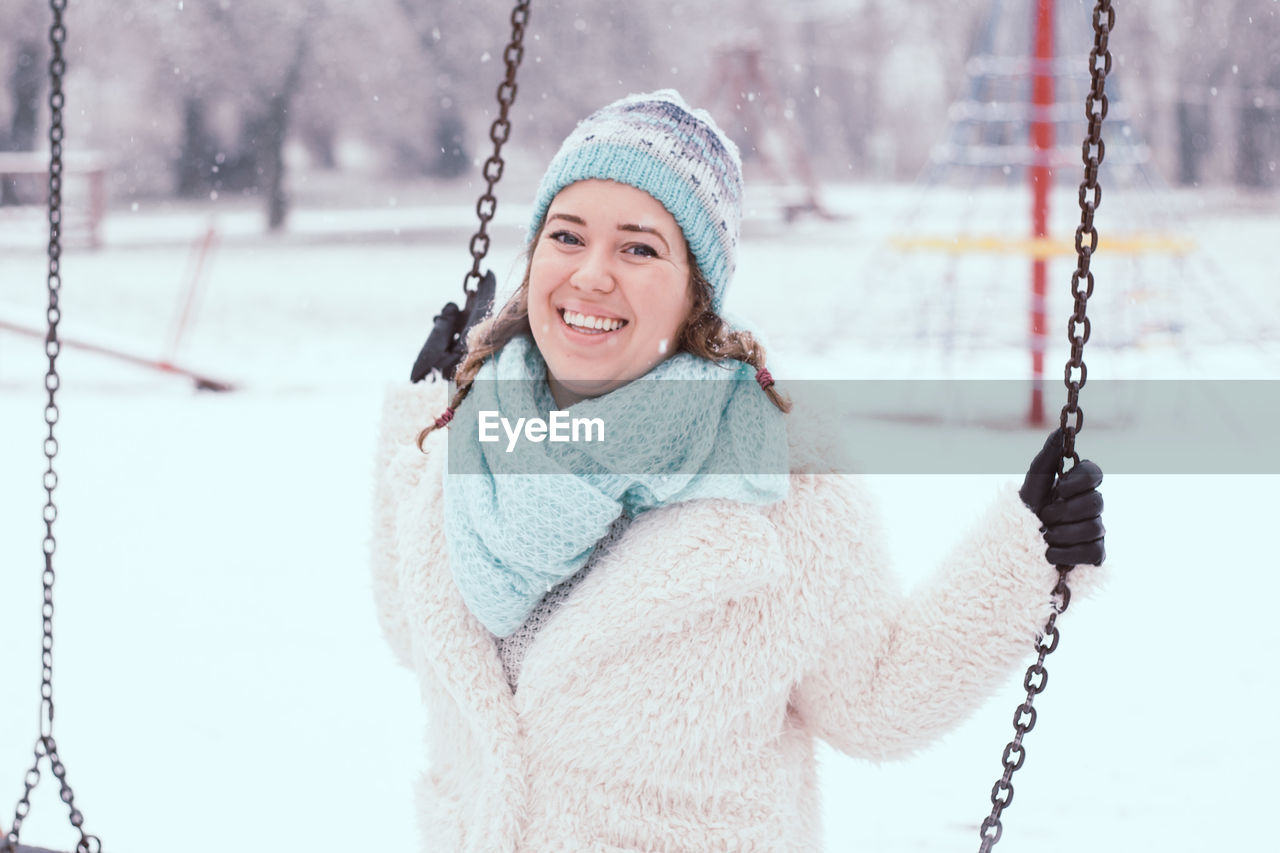 Portrait of happy young woman swinging at park during winter