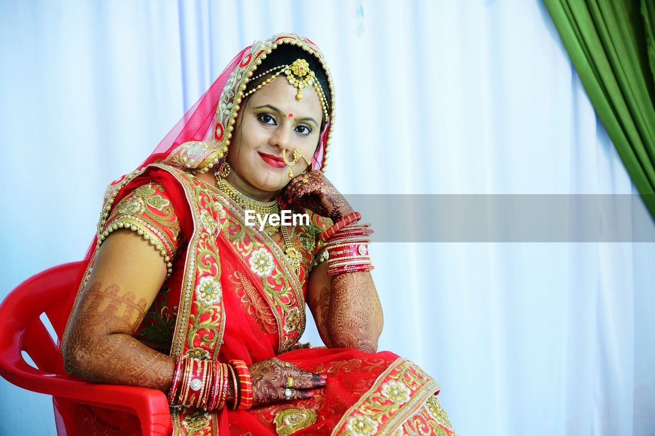 Portrait of bride sitting on chair against white curtain