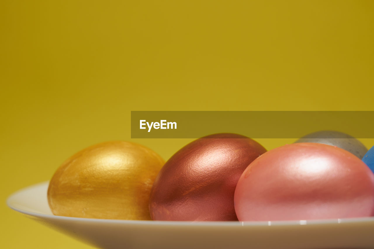 Painted eggs on a white plate with a yellow background.