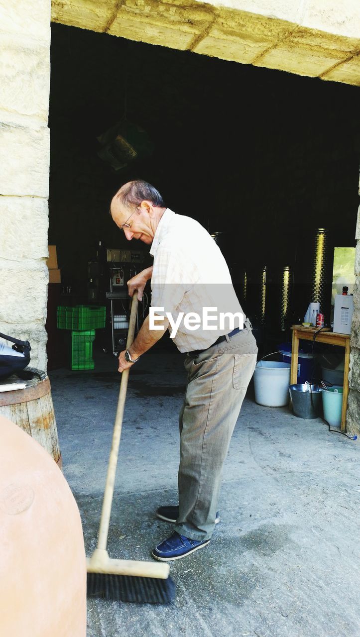 Side view of senior man sweeping floor