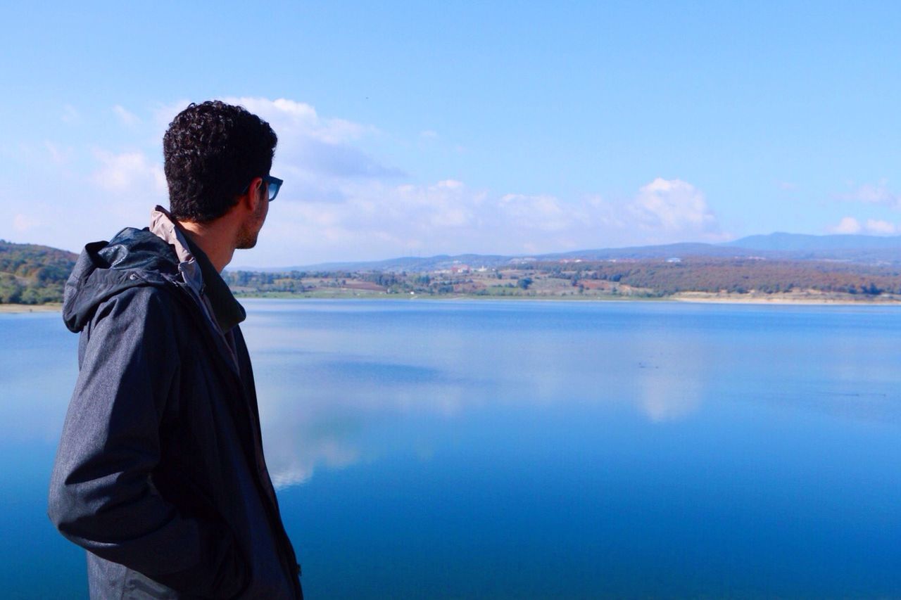 Close-up of man looking at scenic lake against sky