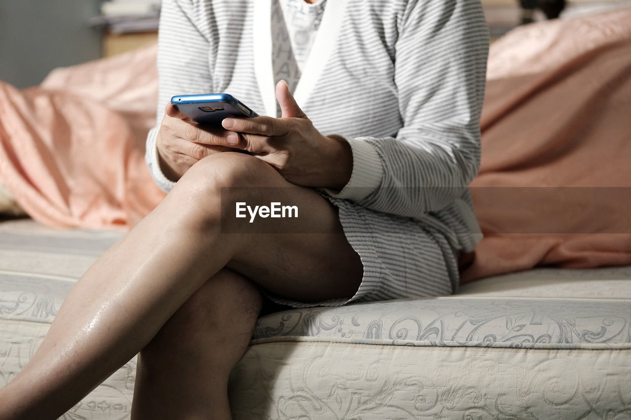 Midsection of woman using mobile phone while sitting on bed